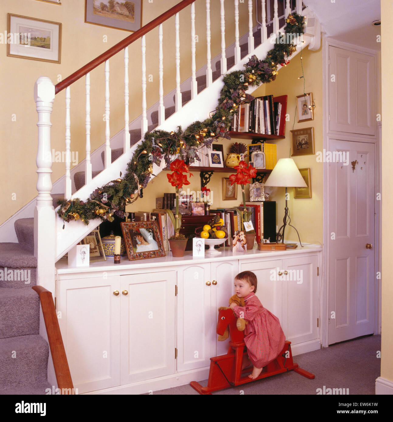 Small girl sitting on a red rocking horse in an nineties hall decorated for Christmas Stock Photo