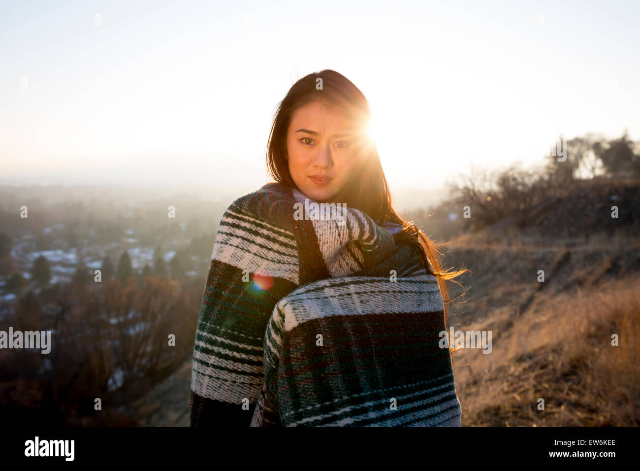 An Asian girl smiles wrapped in a blanket in a small town environment. Stock Photo