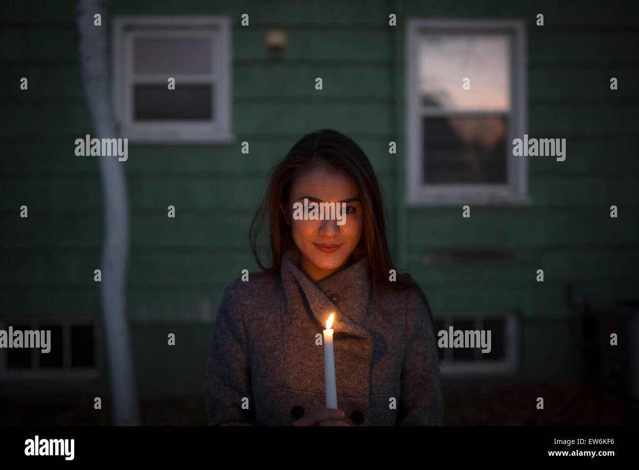 An Asian girl holds a candle in the dark in front of a small house. Stock Photo