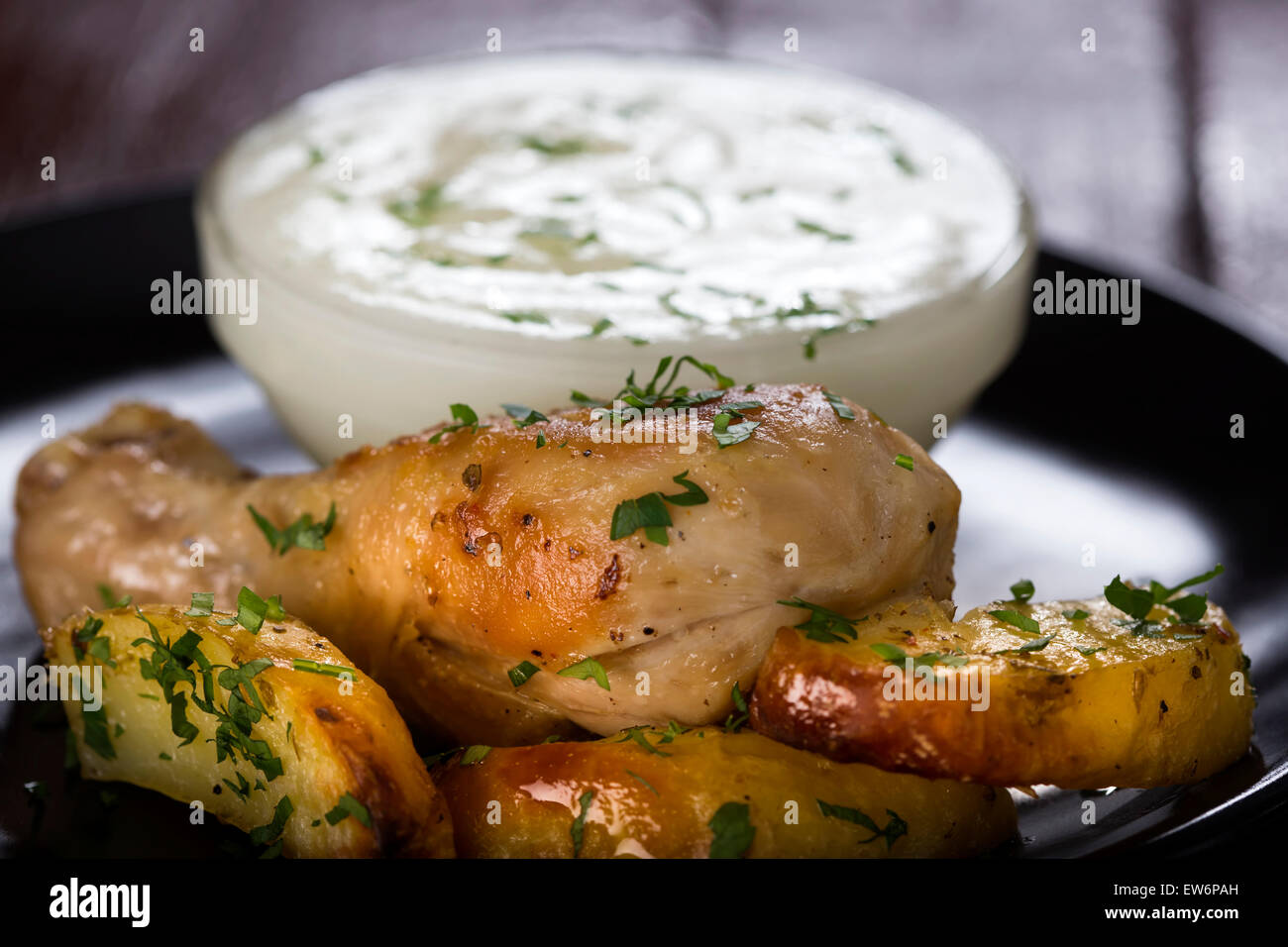 Baked potatoes with roasted chicken drumstick on dark plate Stock Photo