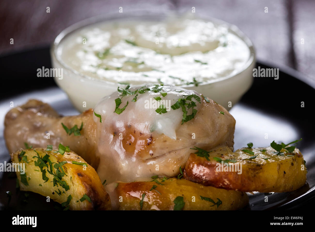 Baked potatoes with roasted chicken drumstick and garlic sauce Stock Photo