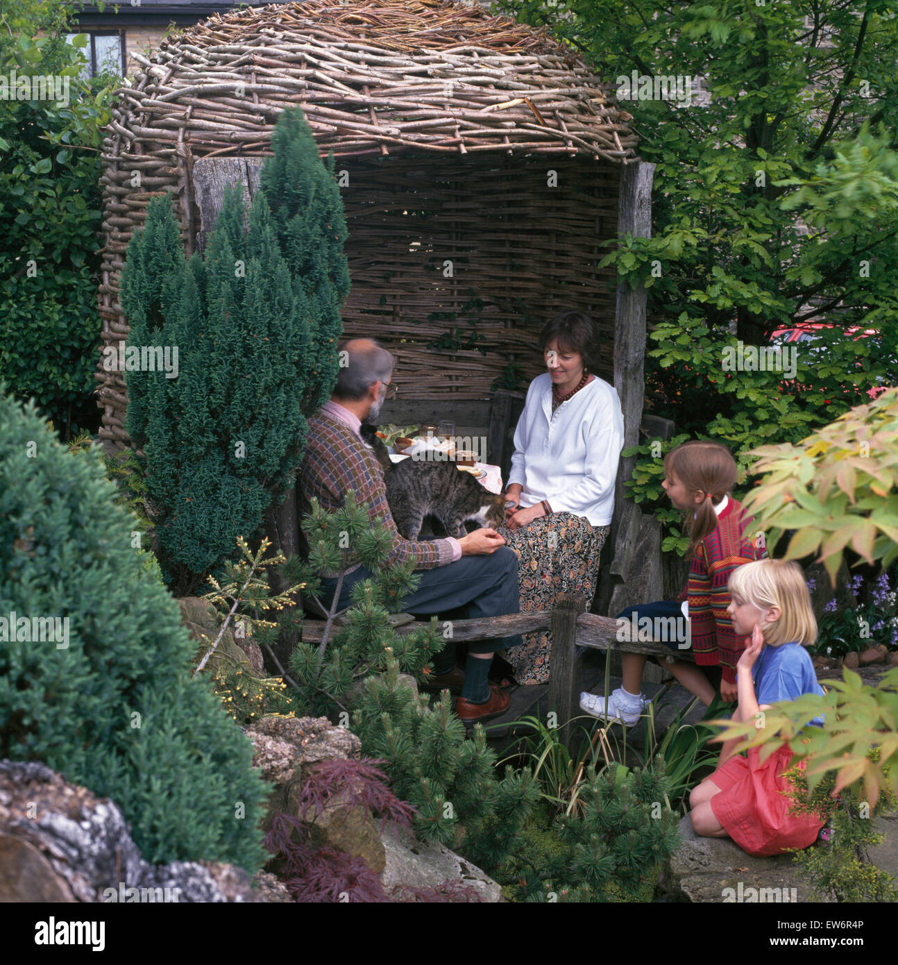 Family sitting beside wicker arbor in garden Stock Photo