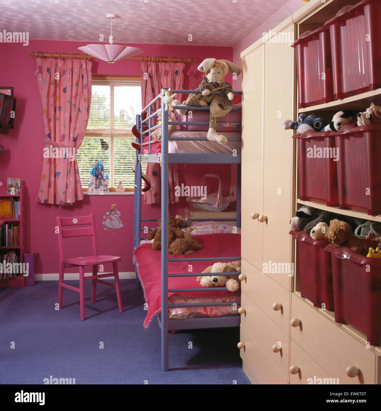 Metal bunk beds in child's bright pink nineties bedroom with plastic storage bins on built in shelves Stock Photo