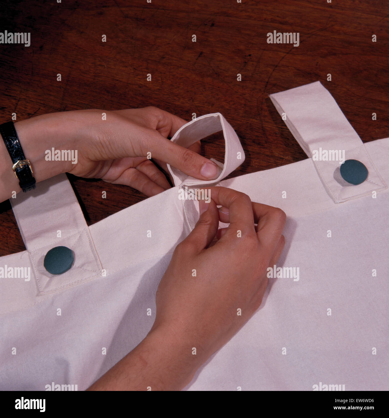 Close-up of hands sewing a white cotton curtain with a tab fastening Stock Photo