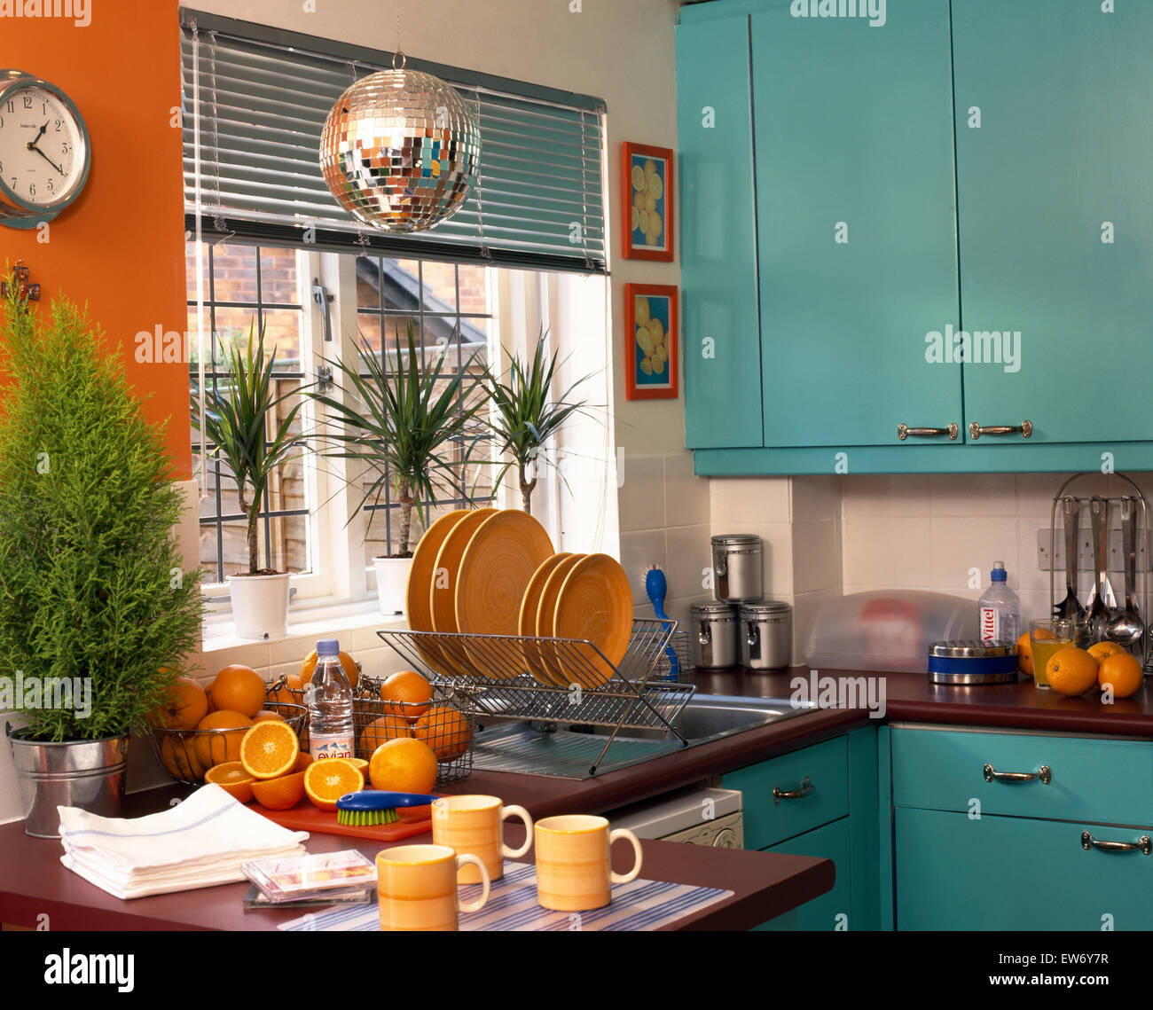 Yellow plates in draining rack beside sink in economy style kitchen with turquoise doors on fitted units Stock Photo