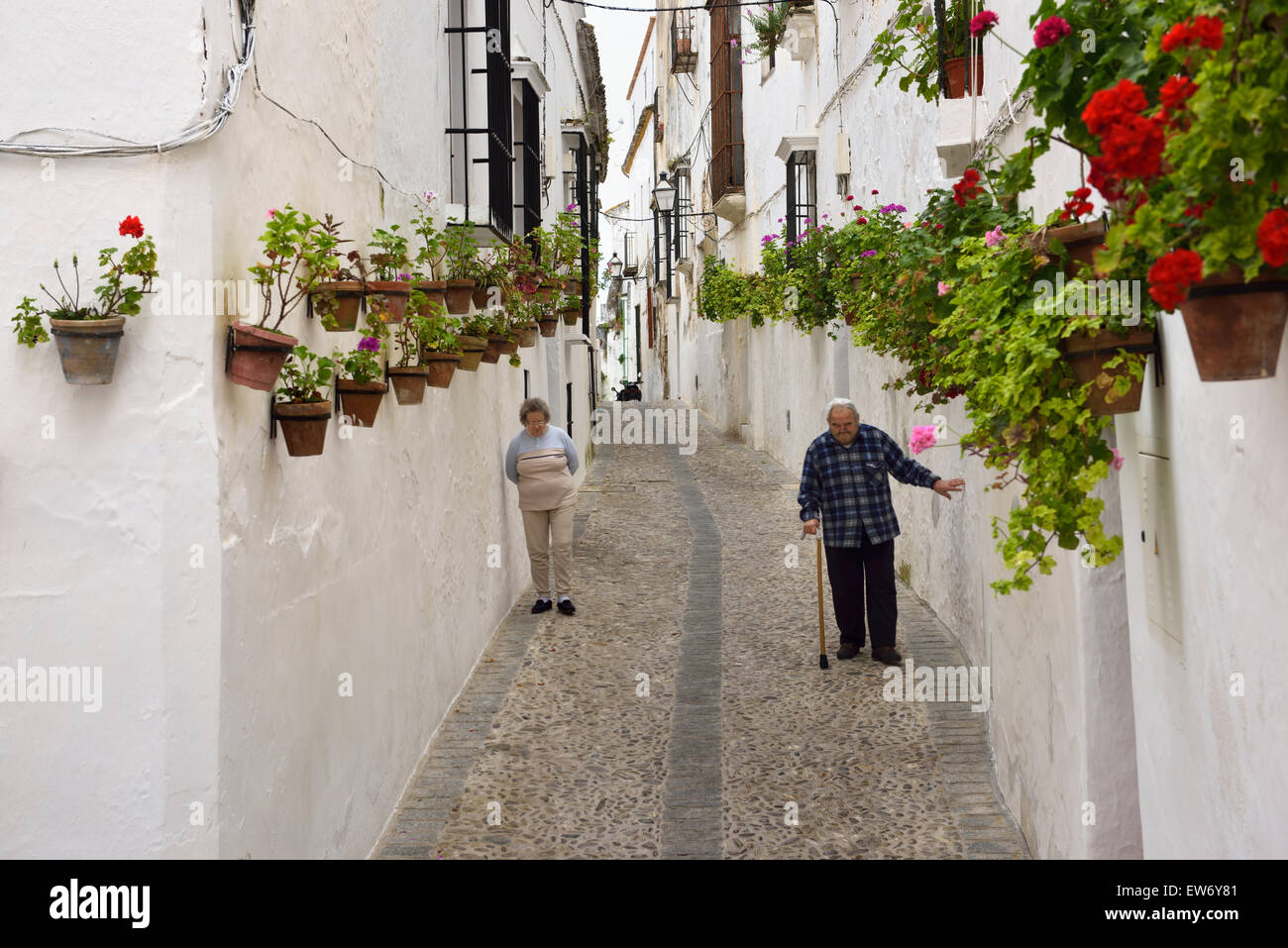 Older couple walking along whitewashed walls with pots of geranium flowers in Arcos de la Frontera Spain Stock Photo