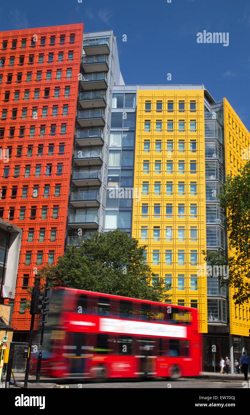 Red London double decker bus passing by brightly colored office blocks Stock Photo