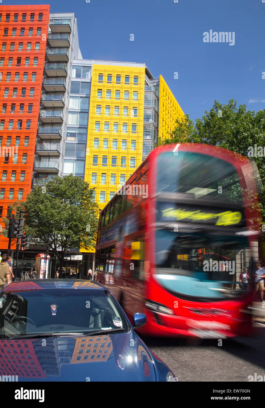 Red London double decker bus passing by brightly colored office blocks Stock Photo