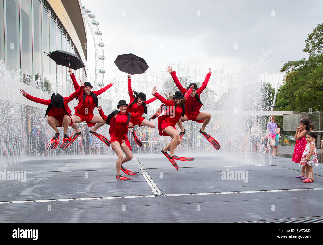 Dancers wearing red costumes and with umbrellas dancing in an artificial rain storm on the Southbank in London Stock Photo