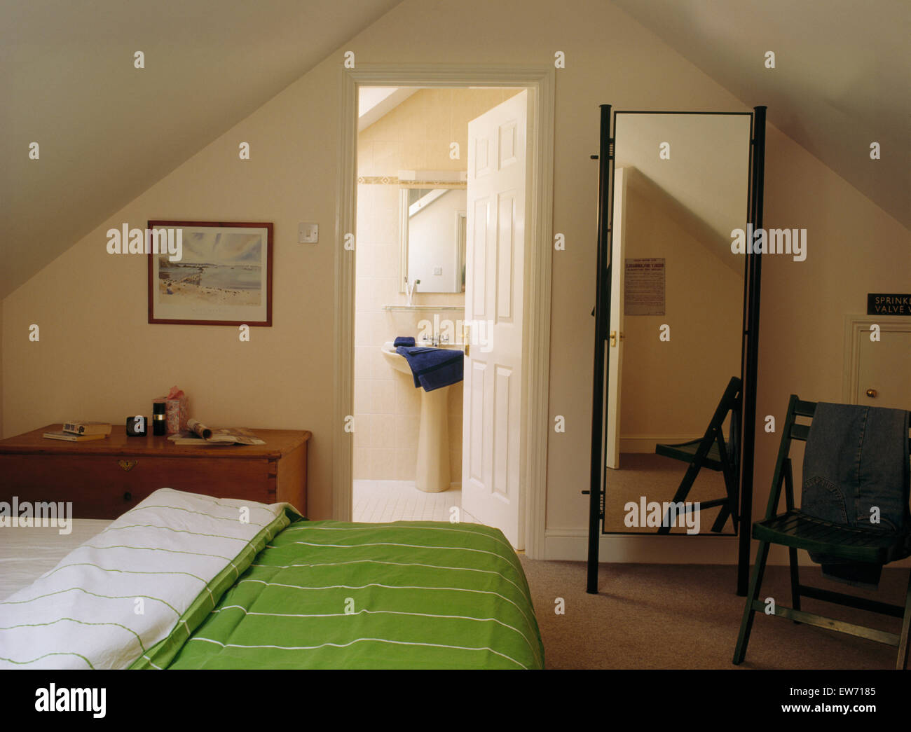 Cheval mirror and bed with green duvet in eighties attic bedroom with door open to en-suite bathroom Stock Photo