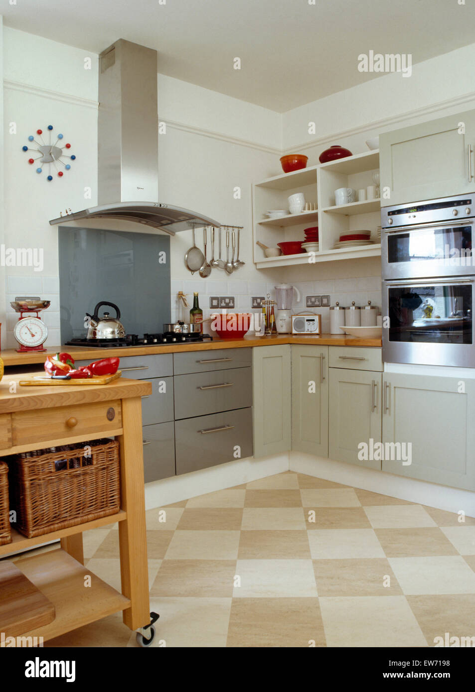 Checkerboard tiled flooring in modern kitchen with stainless steel extractor above hob in gray fitted unit Stock Photo