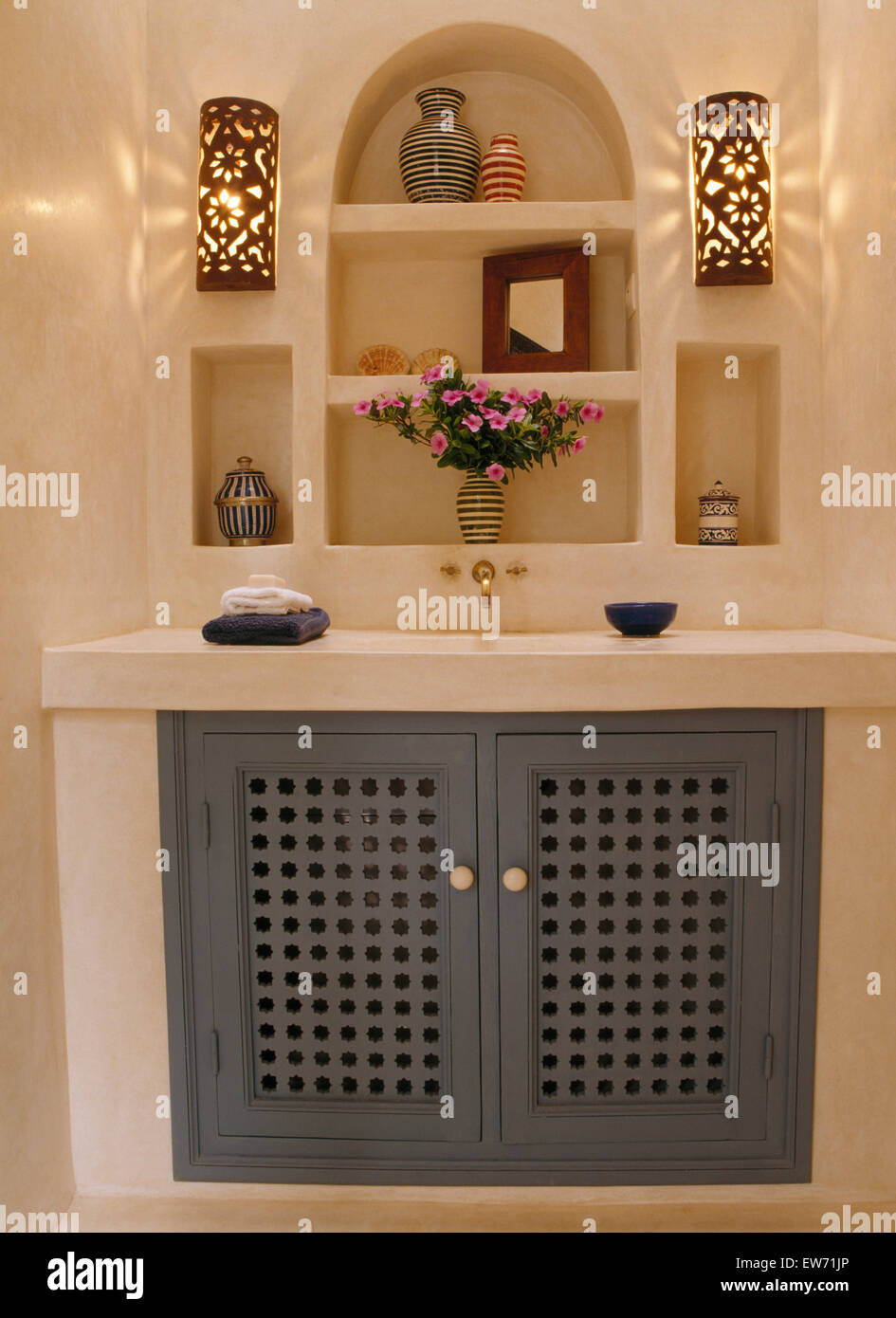 Wall lights on either side of alcove shelves above cupboard with blue fretwork doors in Moroccan bathroom Stock Photo