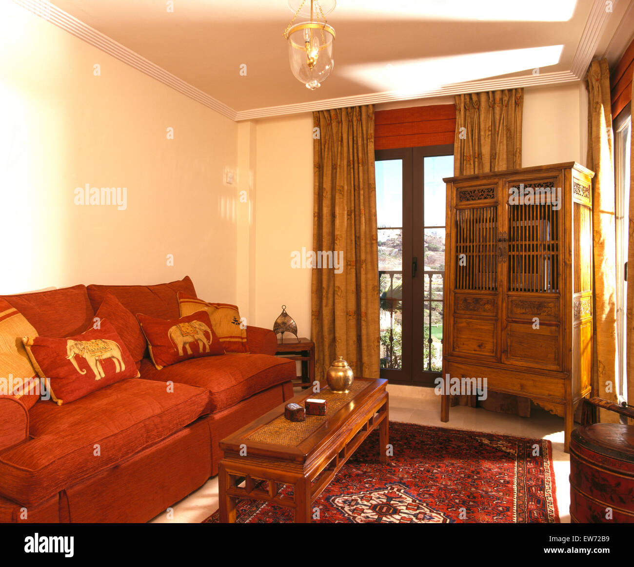 Terracotta colored sofa and traditional carved wooden cupboard in