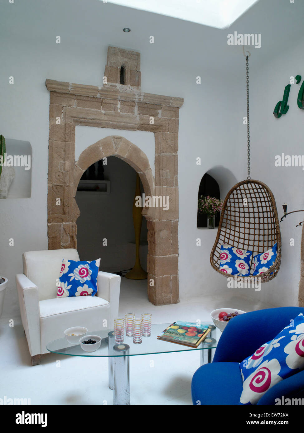 Modern Moroccan living room with white armchair and suspended chair on either side on stone doorway to hall Stock Photo