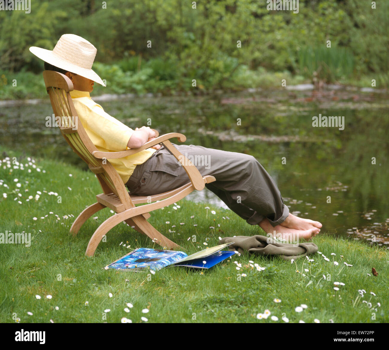 Young man wearing a straw hat sitting and dozing on a wooden lounger Stock Photo