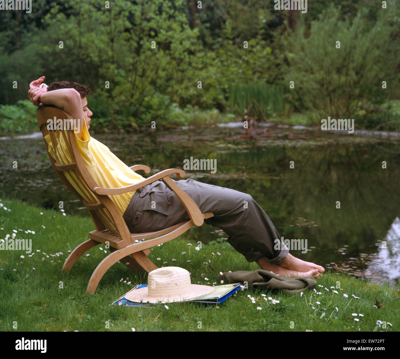 Young man sitting and dozing on a chaise longue beside a garden pool Stock Photo
