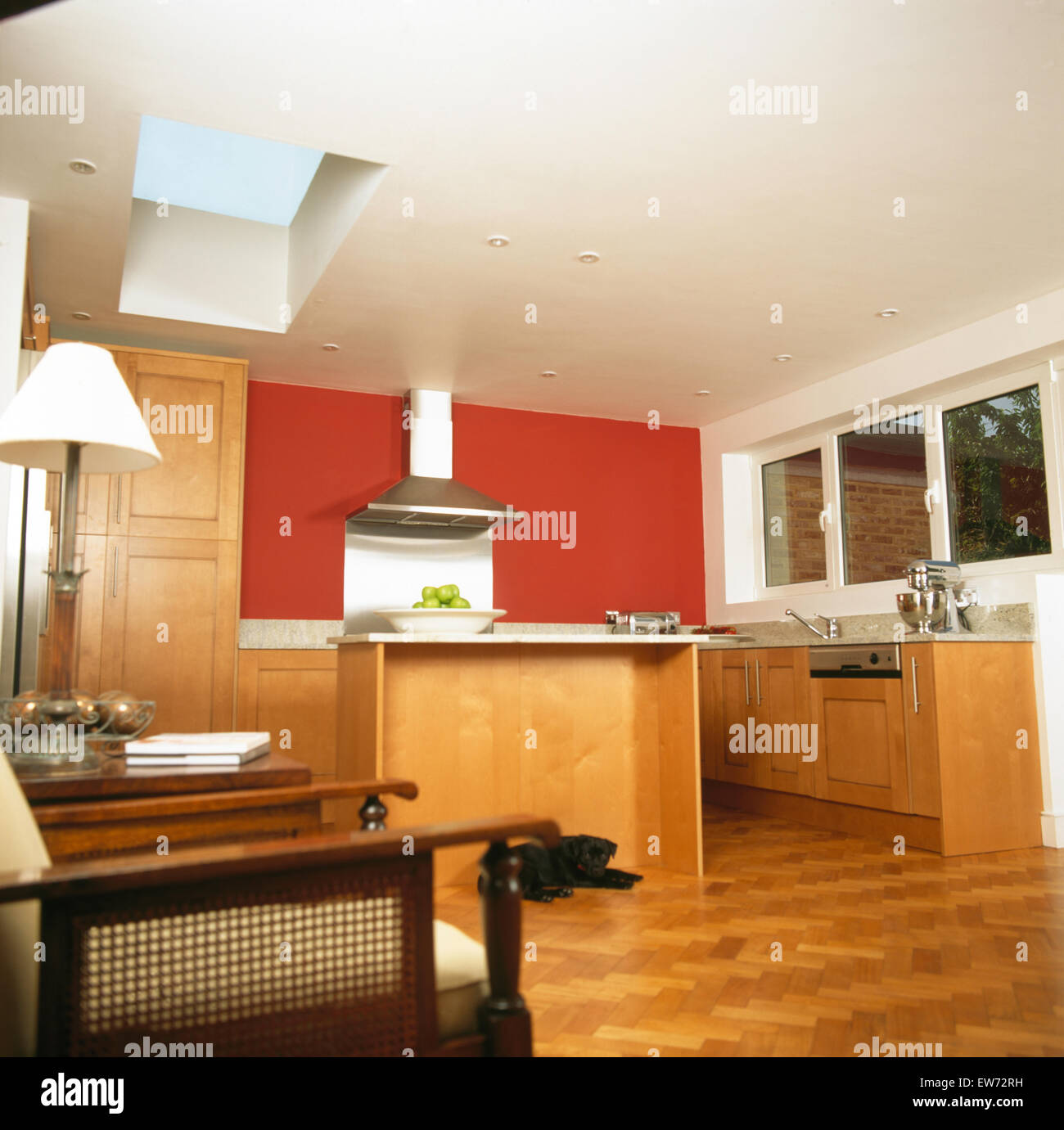 Parquet flooring in modern kitchen extension with red wall and pale wood units Stock Photo