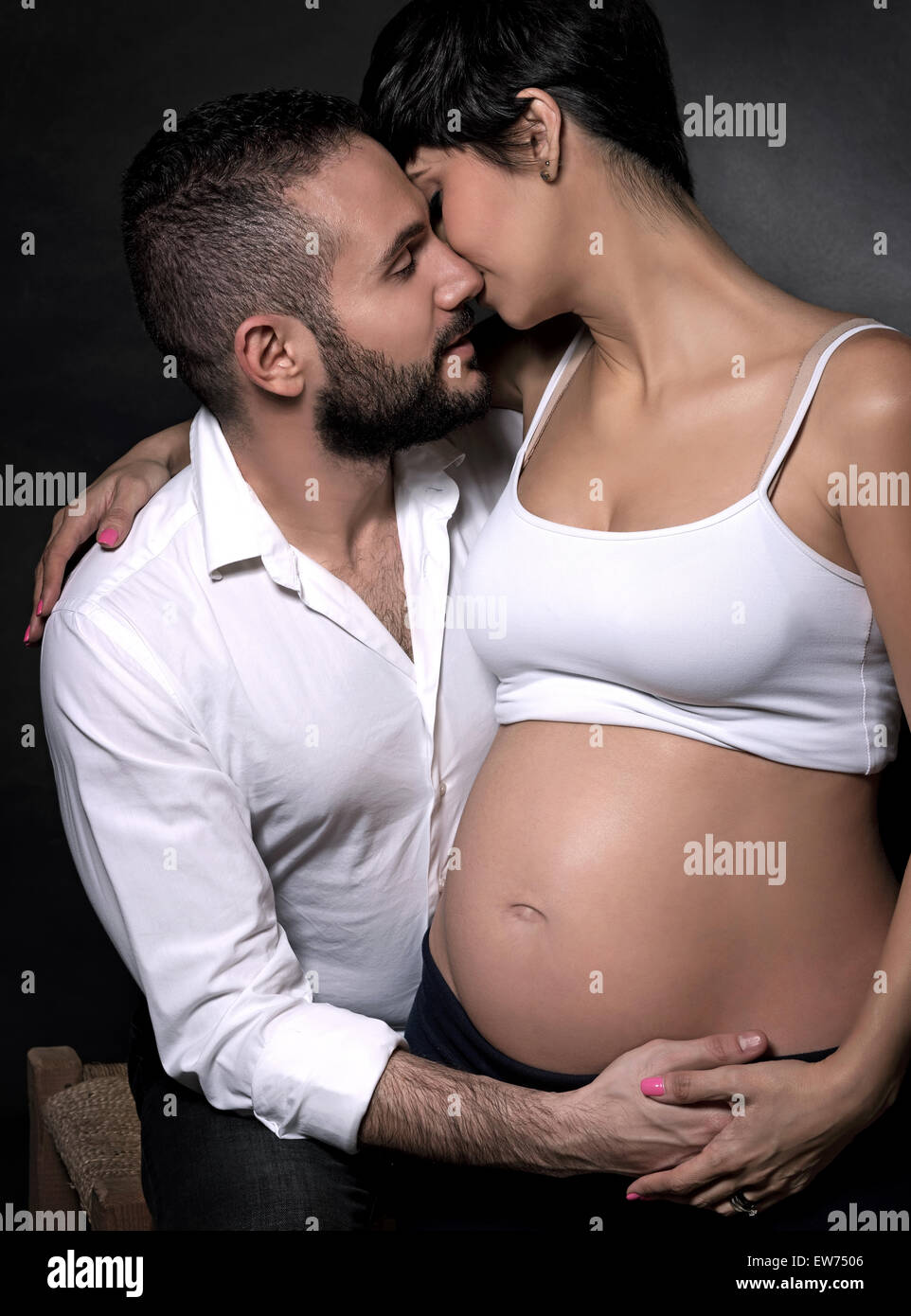 Portrait of gentle romantic couple awaiting baby over black background, happy pregnant woman with husband posing in the studio Stock Photo