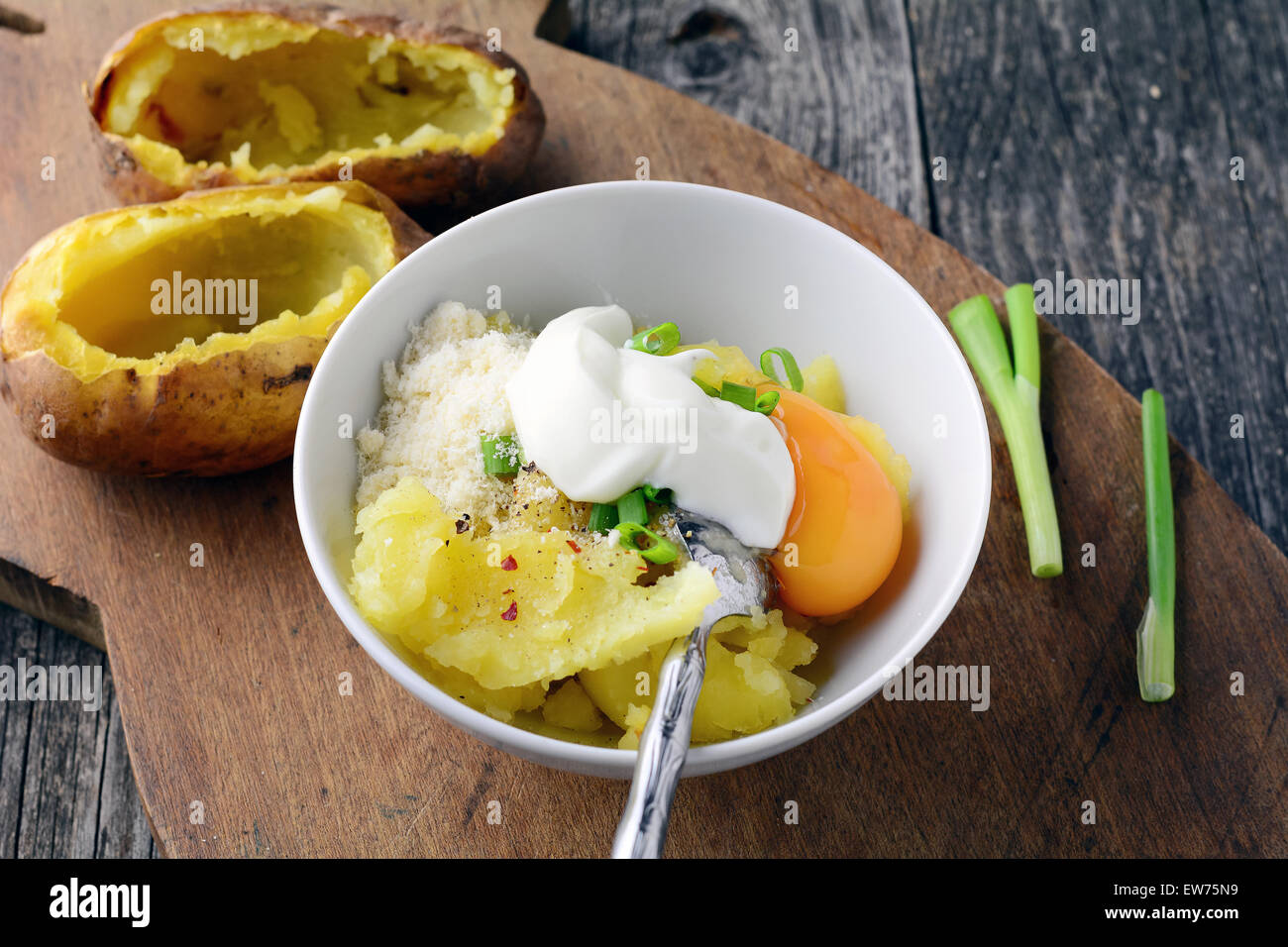 Preparation of jacket potatoes with sour cream, onion, cheese, and egg Stock Photo