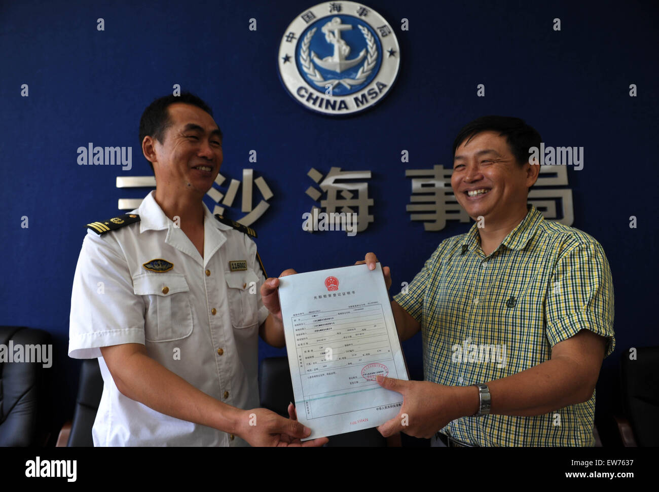 Haikou, China's Hainan Province. 19th June, 2015. A staff member (L) of Sansha Maritime Safety Administration Bureau issues the first certificate of registration of bareboat charter and ship mortgage to an administrative staff of Jiangpeng Sansha Shipping Development Co., Ltd, in Haikou, capital of south China's Hainan Province, June 19, 2015. In order to promote the development of the shipping economy of Sansha, the southernmost city of China, Sansha maritime watchdog opened 'green channel' to streamline the handling process. © Zhao Yingquan/Xinhua/Alamy Live News Stock Photo