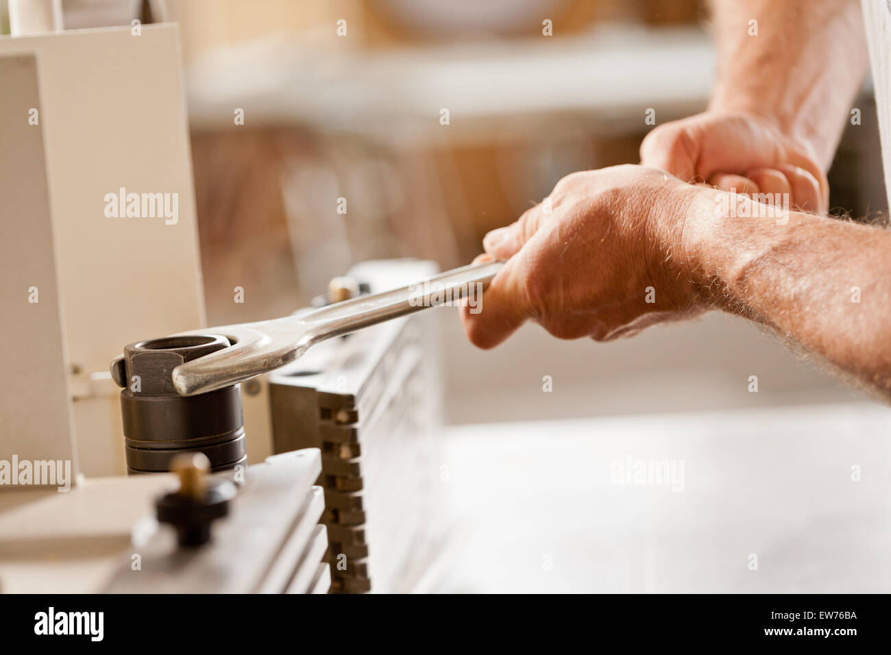 robust carpenter's hands fastening with a wrench in his workshop to adjust a spindle moulder (or wood shaper) Stock Photo