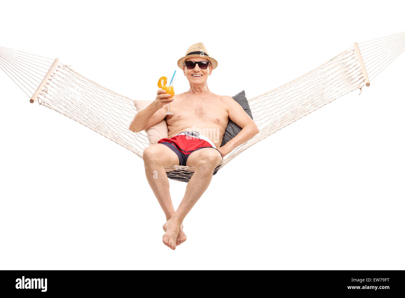 Carefree senior in red swim trunks lying in a hammock and drinking a delicious orange cocktail isolated on white background Stock Photo