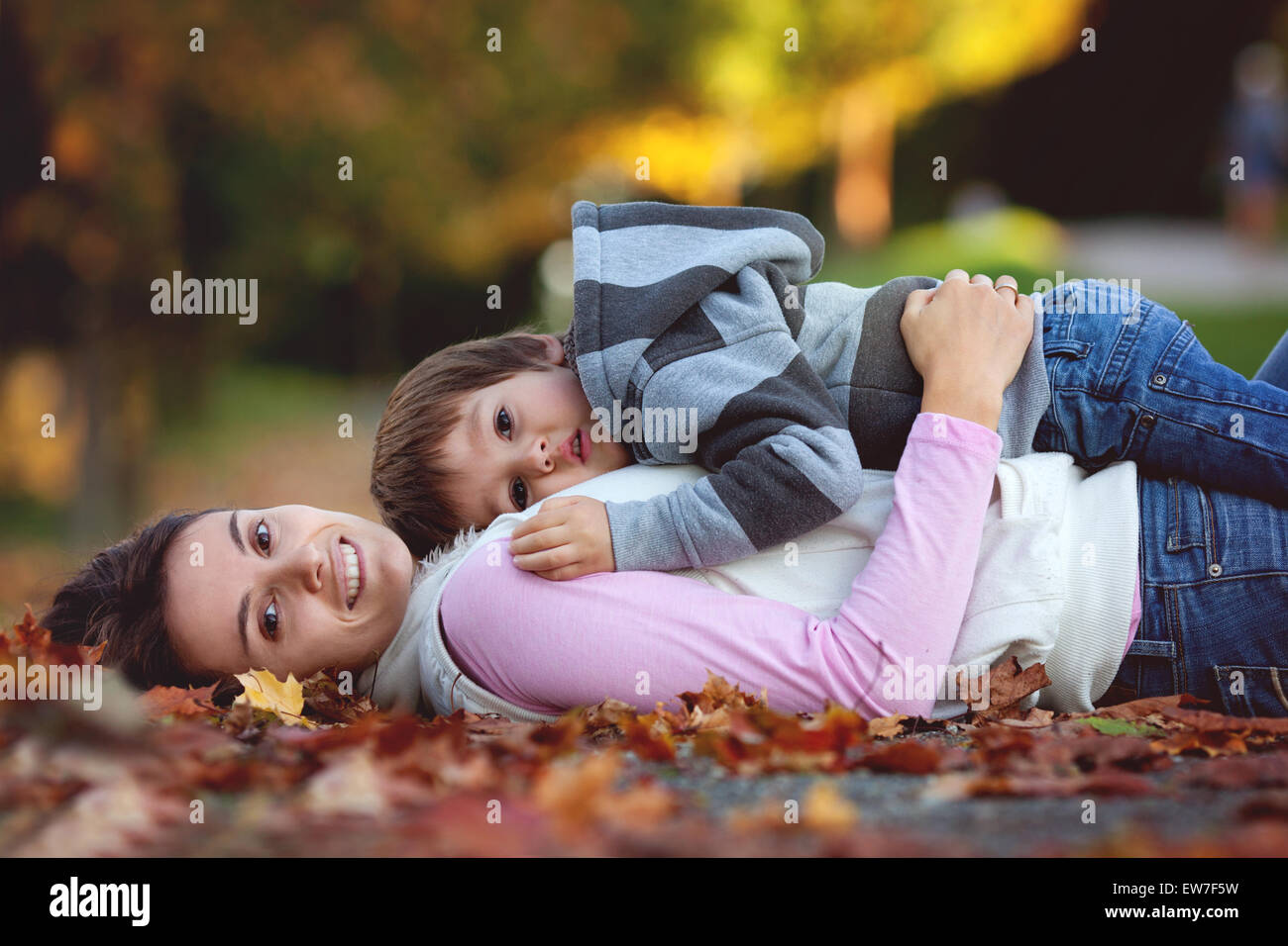 Young mom with her little boy in the park, lying on a path with autumn ...