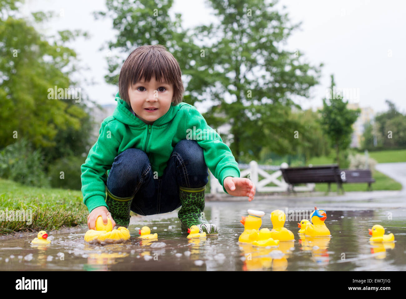 Little boy, jumping and playing in muddy puddles in the park, rubber ducks in the puddle Stock Photo