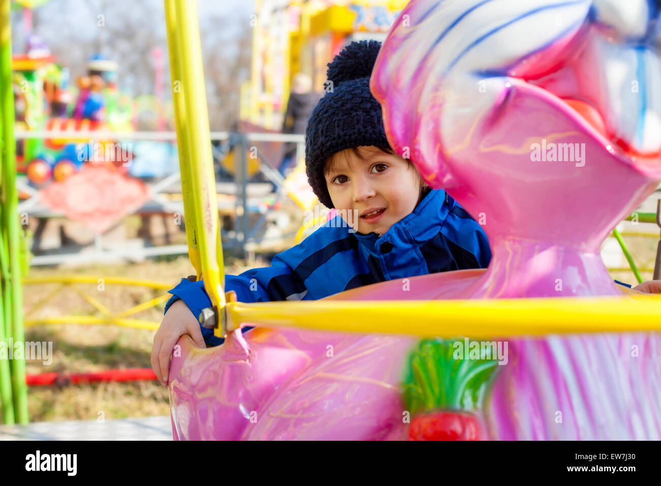 Adorable little boy, swinging on a pink rabbit in amusement park Stock Photo