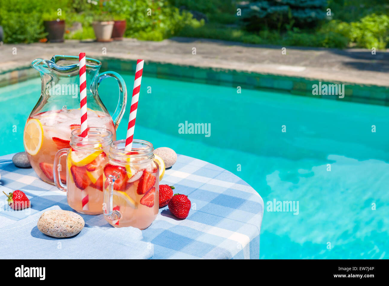 Ice cold homemade strawberry lemonade in jug and glasses with paper straws on outdoor summer pool side table plus copy space Stock Photo