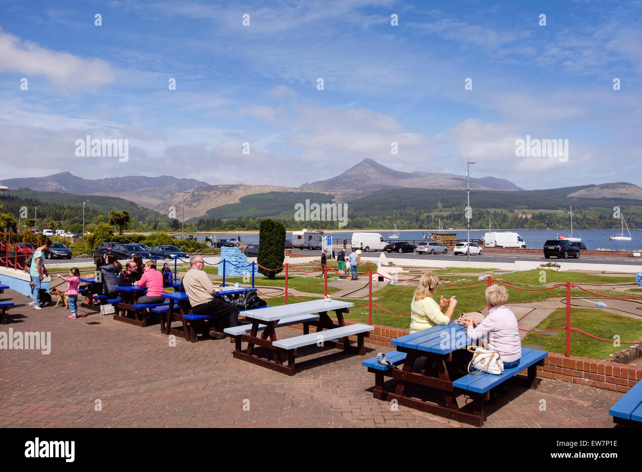 People sitting outside Little Rock cafe with a view to Goat Fell mountain across Brodick Bay on a sunny day. Brodick Isle of Arran Scotland UK Stock Photo