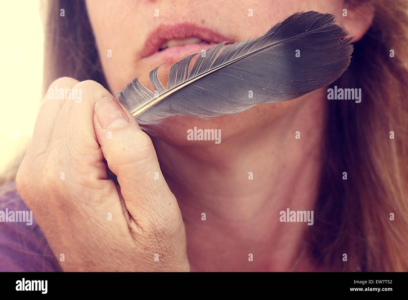 Close up of a woman holding a feather close to her face Stock Photo