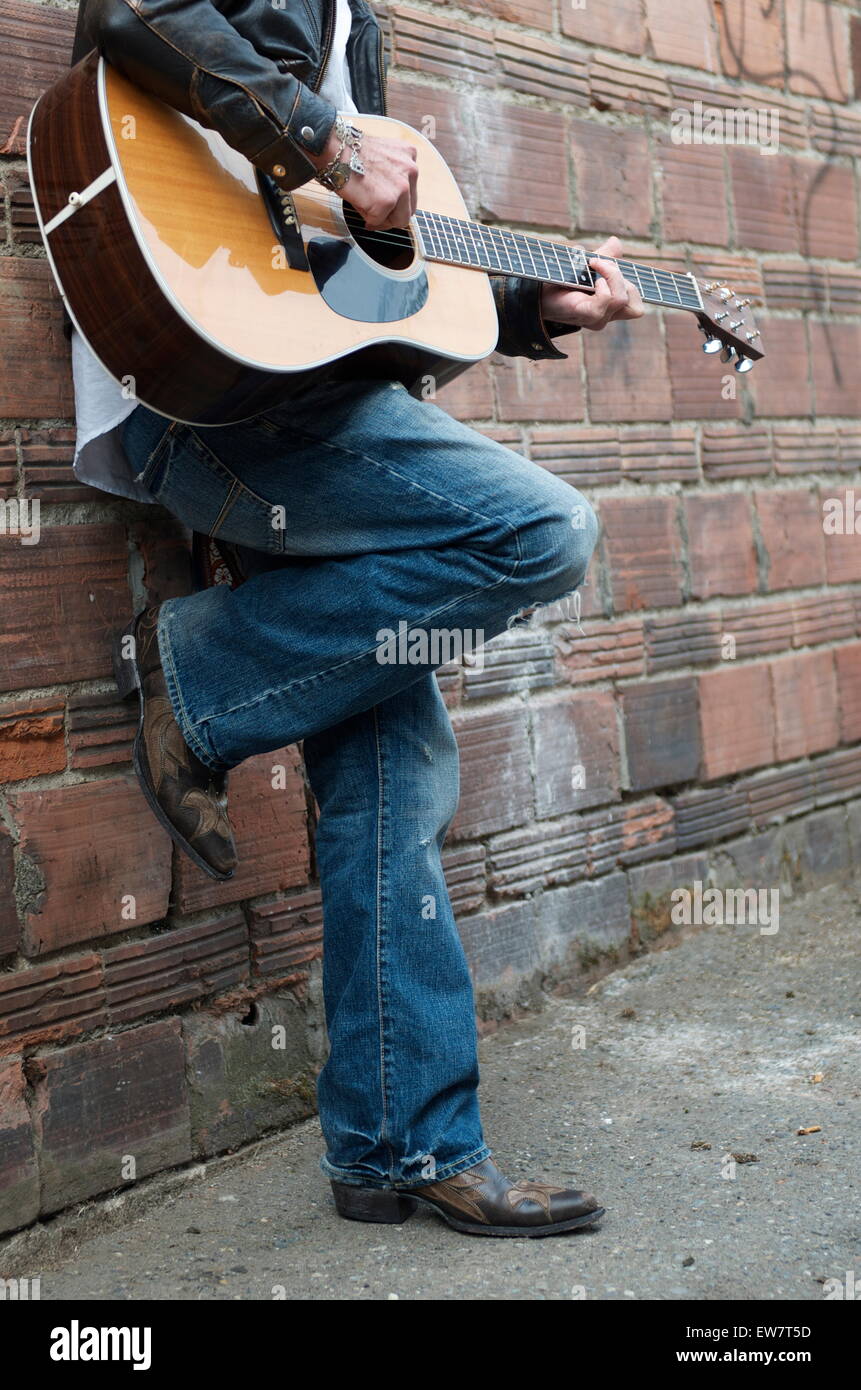 Man in Leather Jacket and Cowboy Boots Playing the Guitar in an Alley Stock Photo
