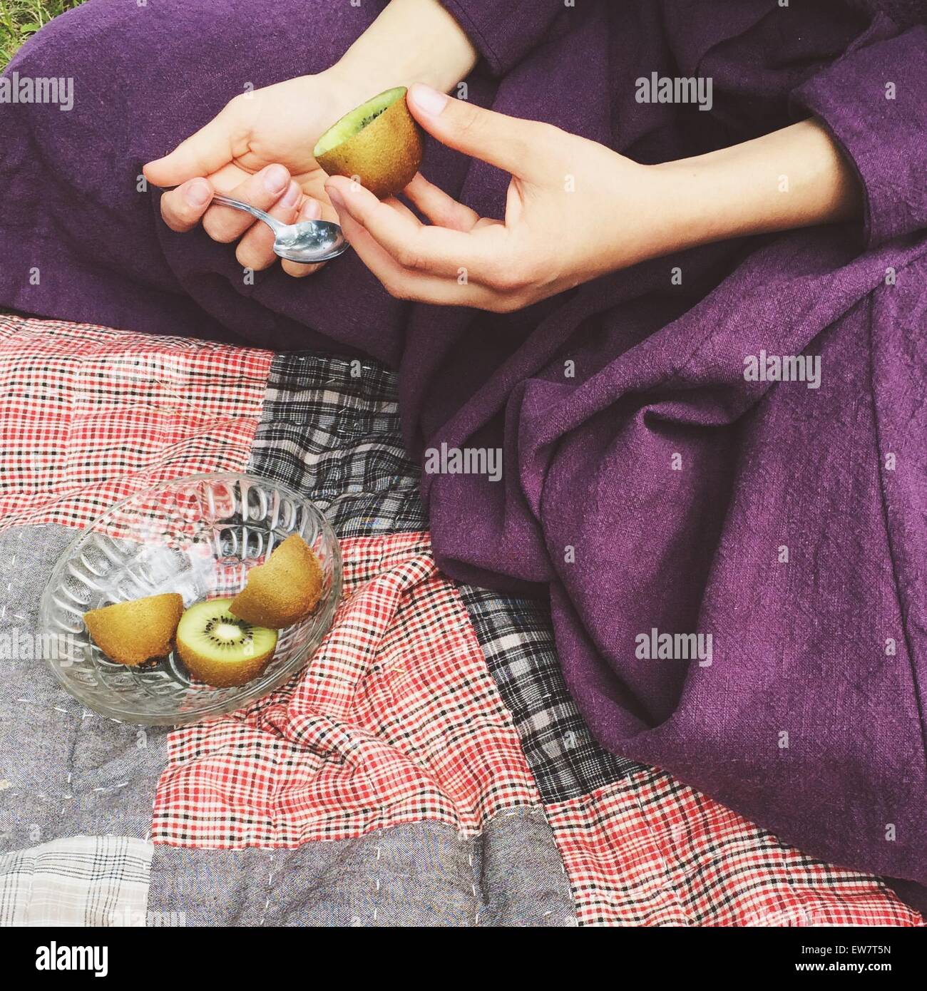 Close-up of a woman sitting on a rug eating a kiwi fruit Stock Photo