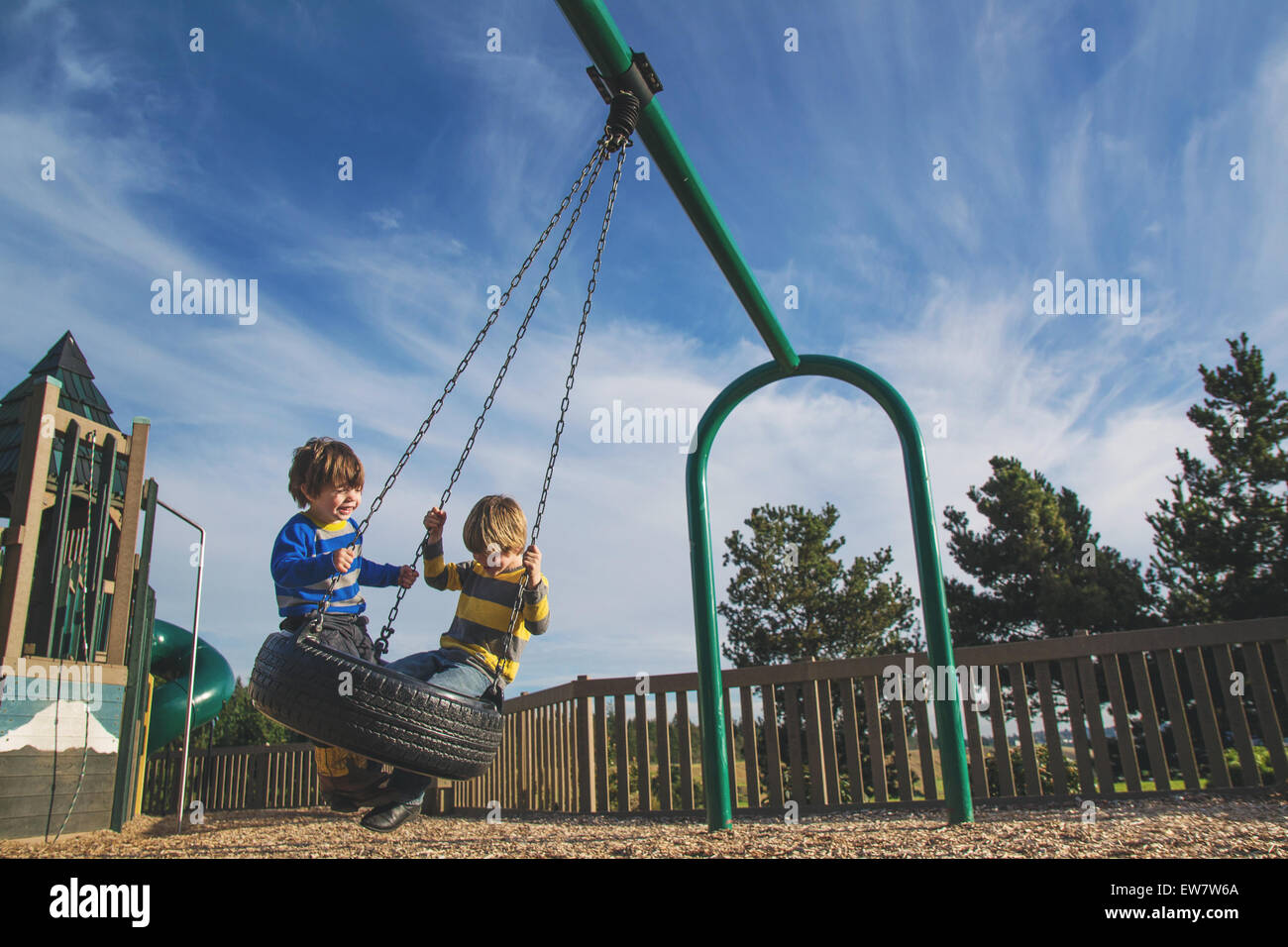 Two young boys swinging on a tire swing at a park Stock Photo