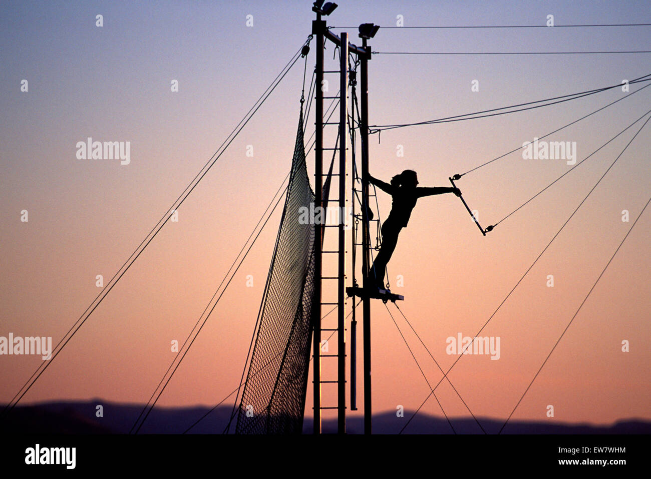 Woman swinging on a trapeze at sunset (silhouette). Stock Photo