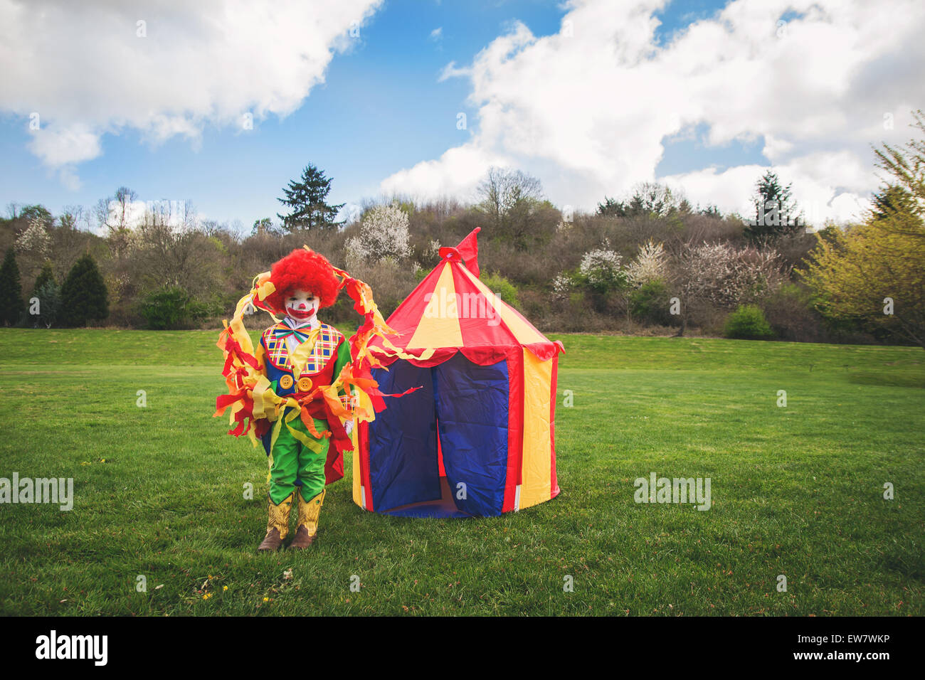 Boy dressed as a clown standing in front of a toy circus tent Stock Photo