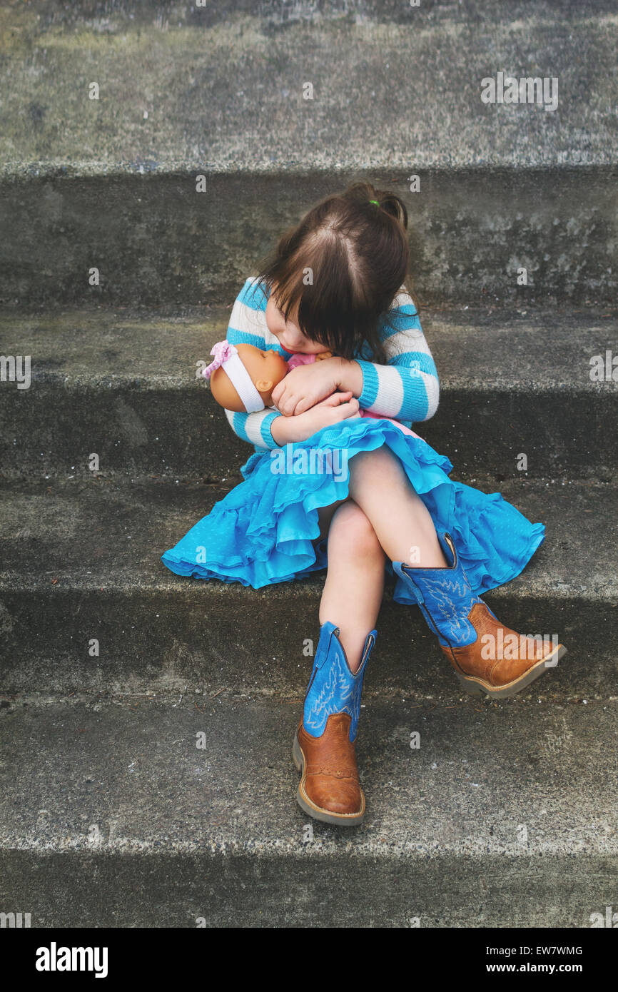 Girl sitting on a step hugging a baby doll Stock Photo