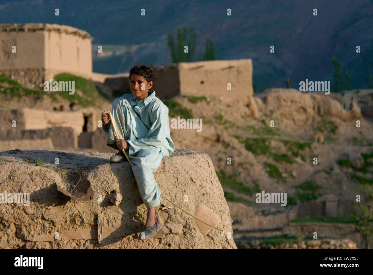 A boy sits on a mud wall in the Tajik village of Dera Jawal, at the base of the Band-e Baba range,  Herat Province Stock Photo