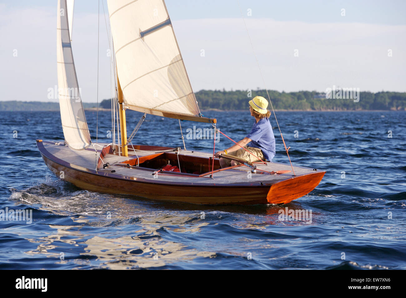 A teenage boy steers a classic wooden sailing dinghy under sail on a