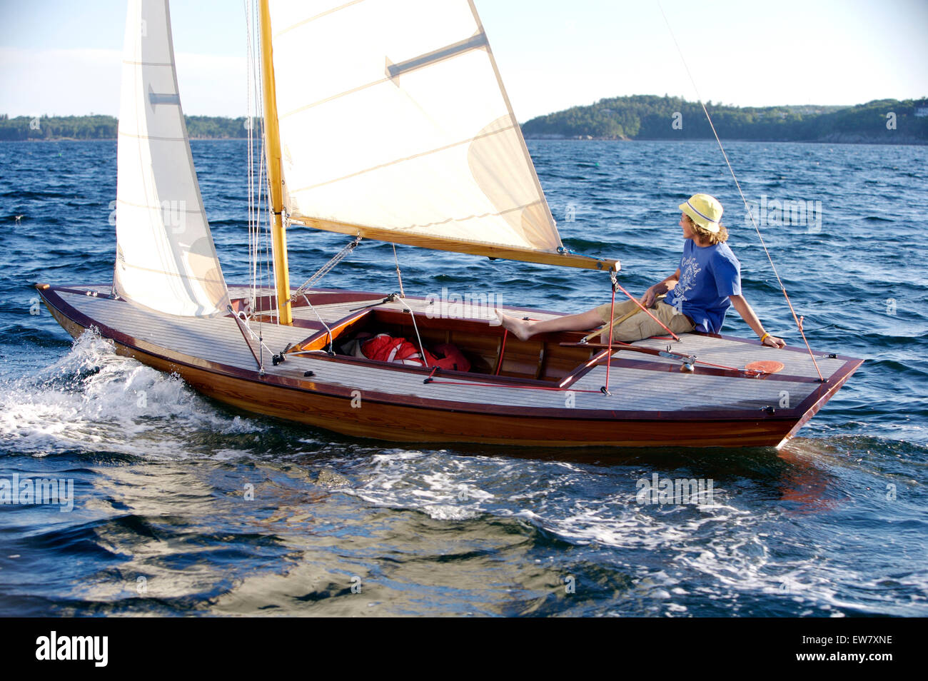 A cheerful teenage boy sails a beautiful wooden dinghy in the late afternoon sun, on Penobscot