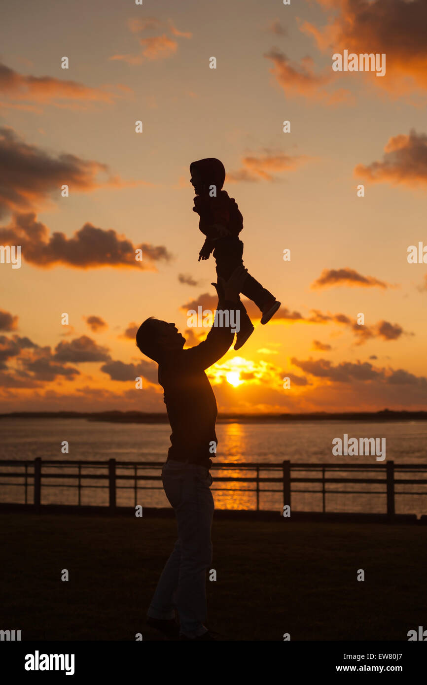 Father throwing his kid up in the air on the beach, silhouette shot on