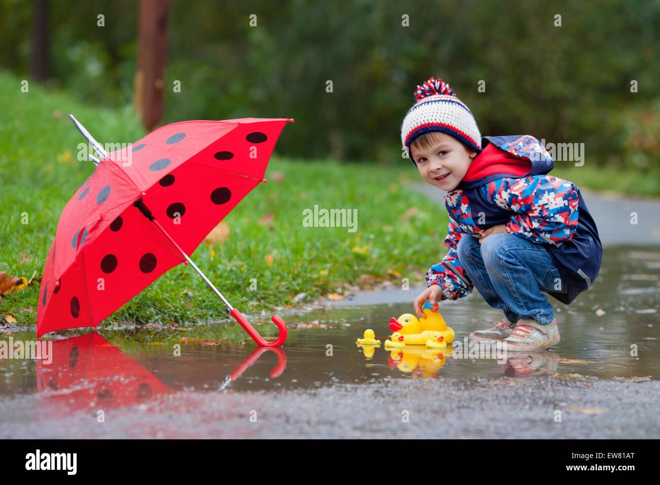 Cute boy with hat, playing with rubber ducks in the park in a puddle Stock Photo