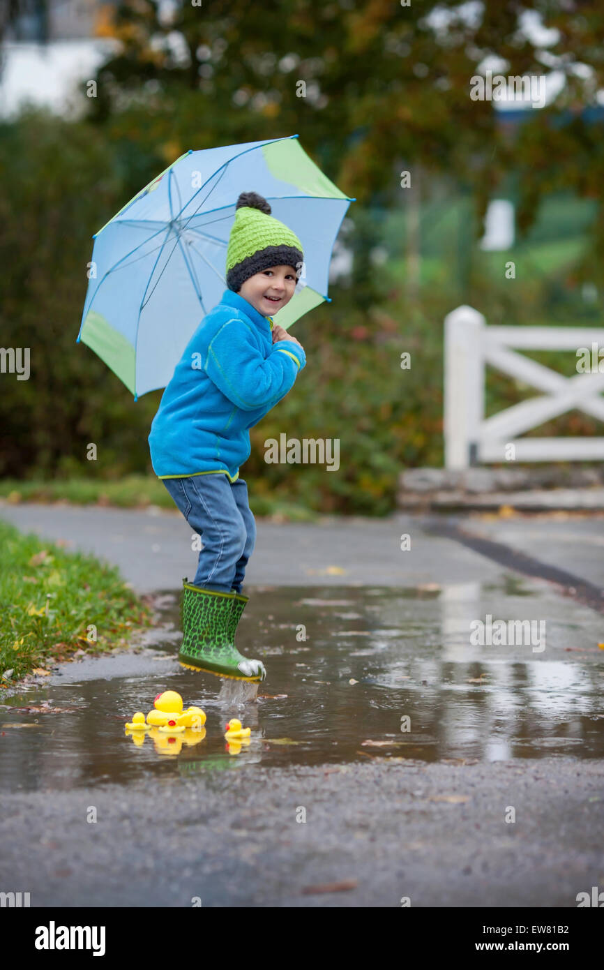 Little boy, jumping in muddy puddles in the park, rubber ducks in the puddle Stock Photo