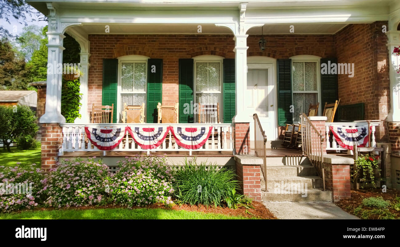 front porch of a brick home in a small American town with patriotic flags and rocking chairs Stock Photo