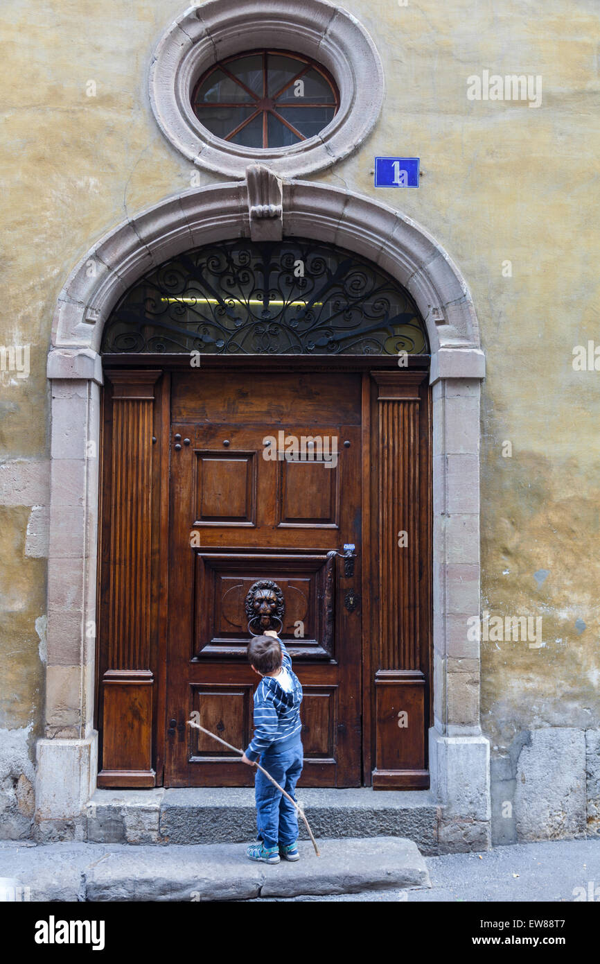 Young boy knocking on a large door in the old town of Geneva, Switzerland Stock Photo