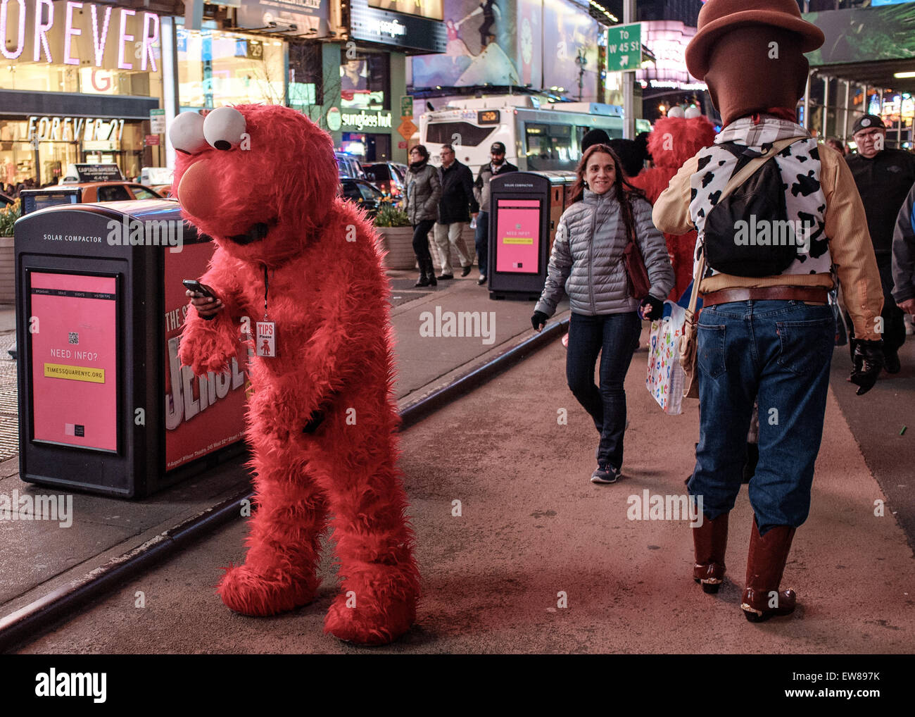 Times Square NYC  , Street performers Elmo ( on his Smartphone ) and Pixars Woody (walking away .Female tourist with an  amused Stock Photo