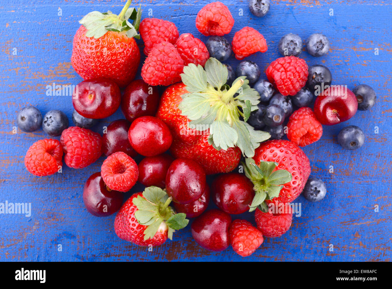 Summer fruit with raspberries, blueberries, strawberries and cherries on dark blue wood table. Stock Photo