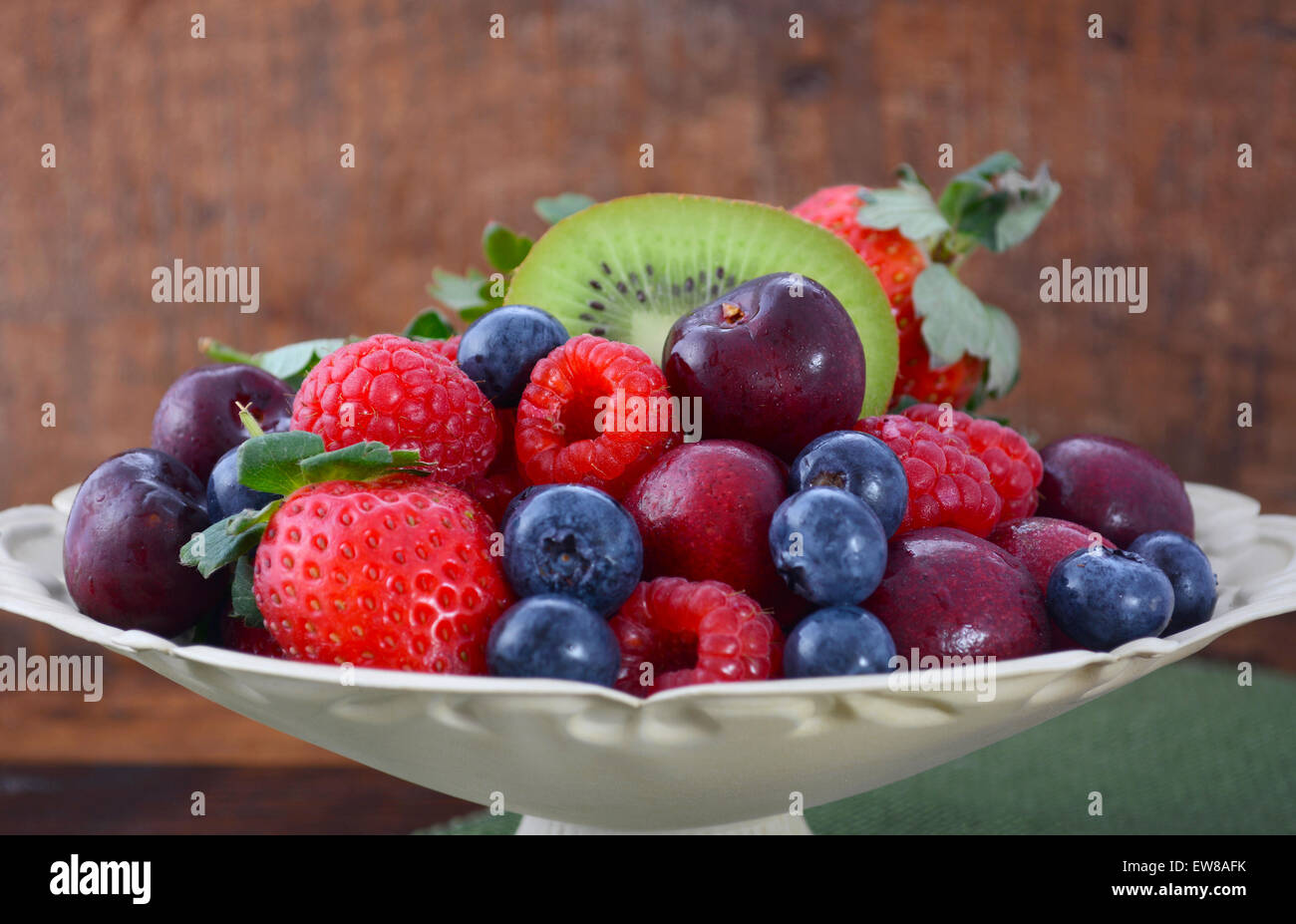 Summer Fruit including raspberries, strawberries, cherries, blueberries and kiwi fruit in a vintage bowl with reclaimed dark woo Stock Photo