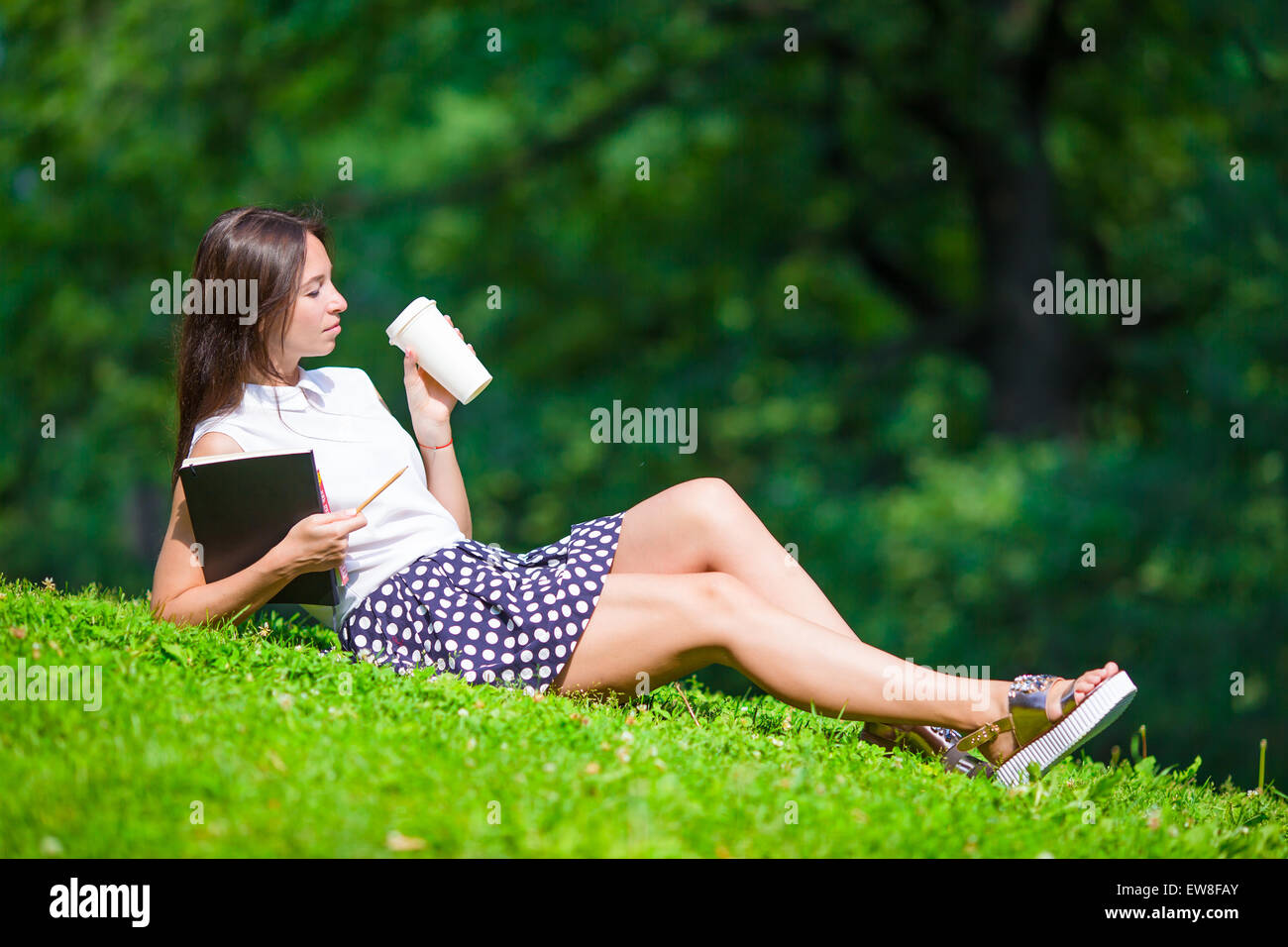 Young woman relaxing with coffee in park reading a book Stock Photo - Alamy